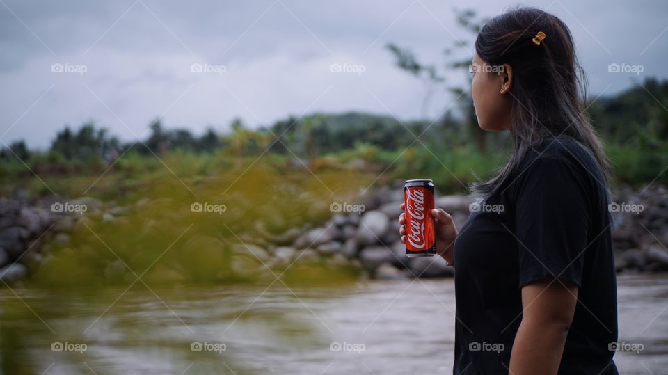 A long-haired woman is holding a can of coca cola