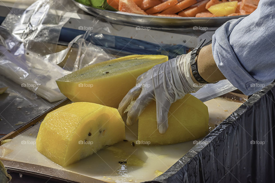 Hand holding yellow watermelon And use a knife to cut a piece.