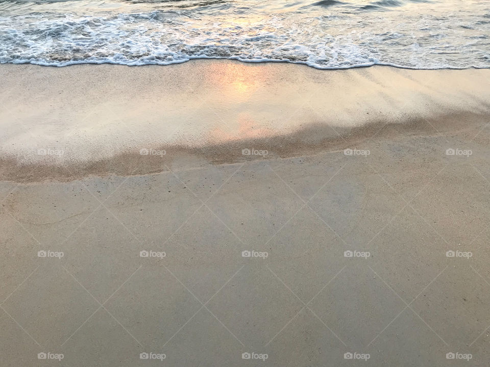 crystal clear sand beach with sea wave and sunset light reflection