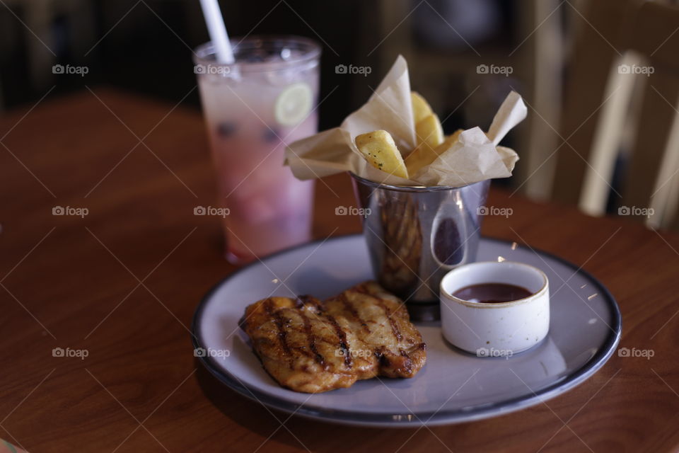 Delicious grilled chicken BBQ and french fries served on plate and refreshing frozen berry juice at a restaurant