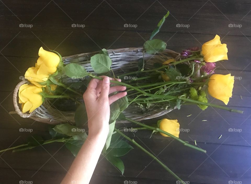 Woman creating a Floral arrangement in a basket with yellow roses 