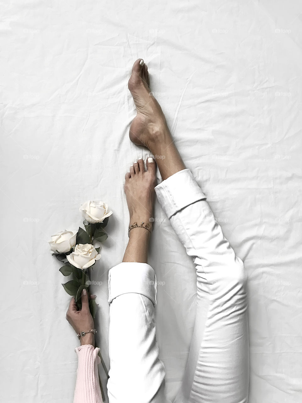 Overhead view of female legs in white denim jeans and hand holding white roses in bed