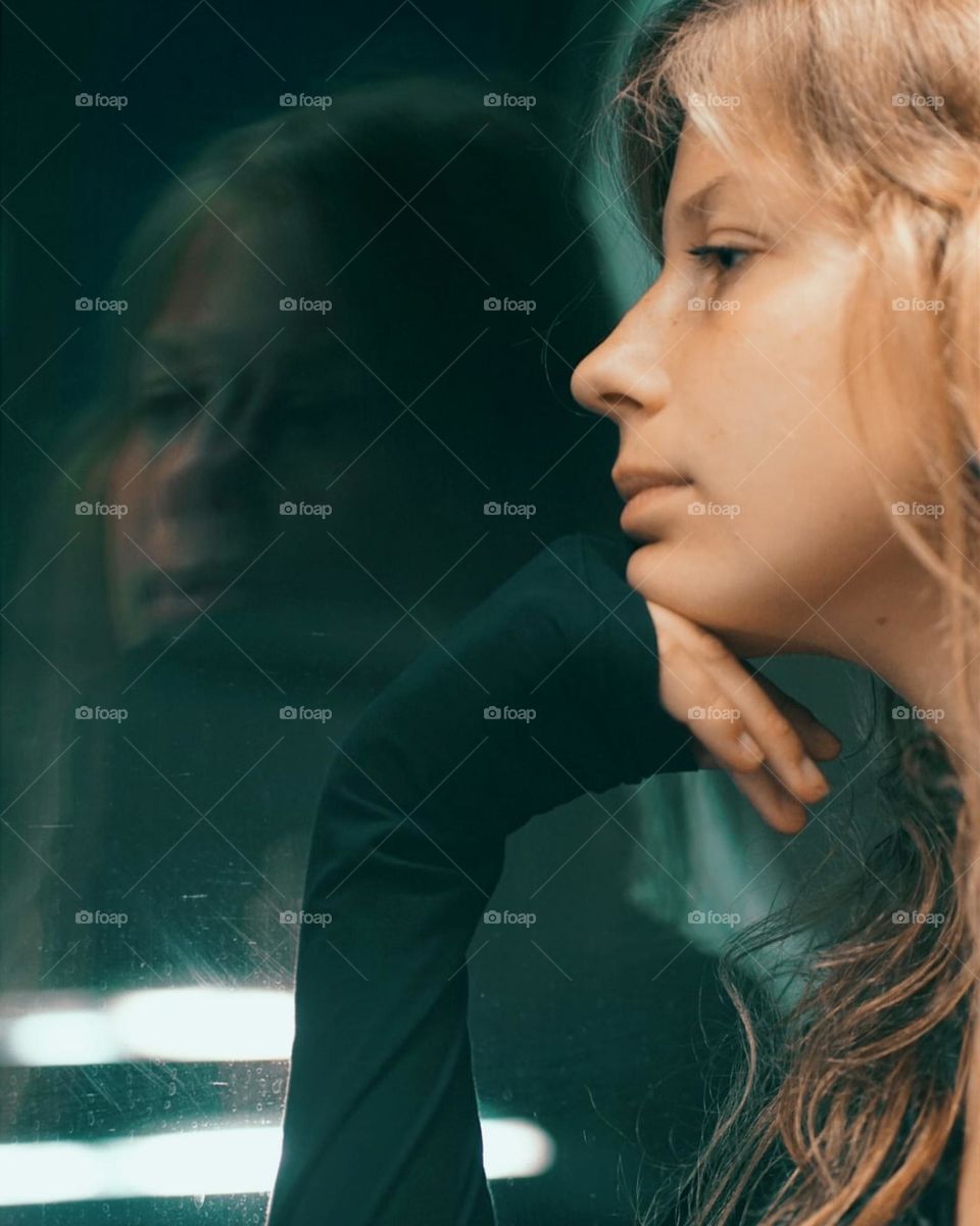 young blonde woman looking at her reflection in the window on a train