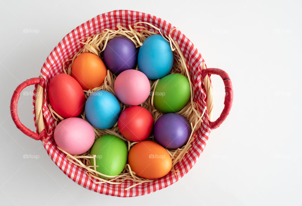 Colorful Easter eggs in a basket with straw isolated on white background. Shot from above shot.