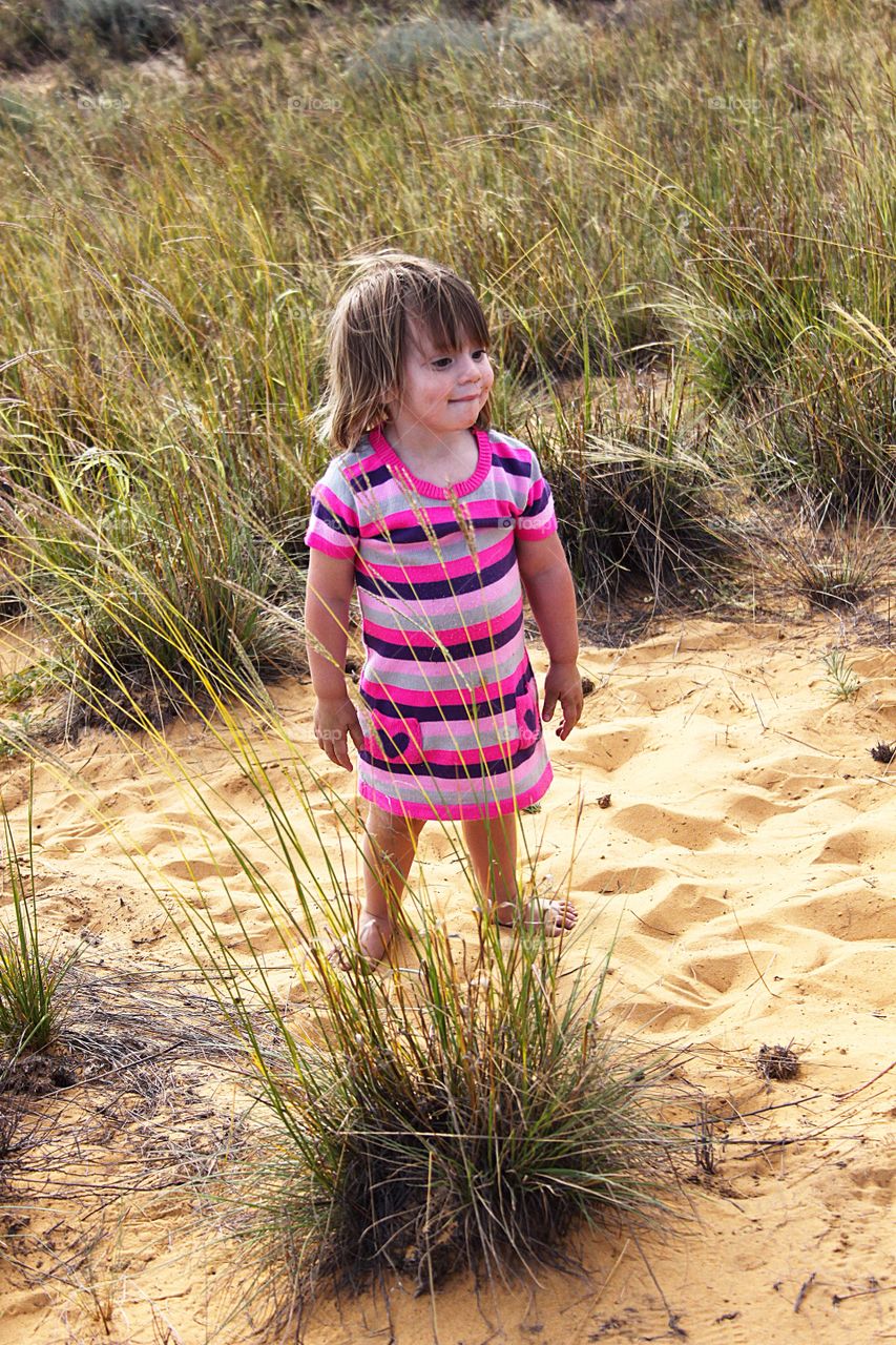 Expressive little girl standing on sand