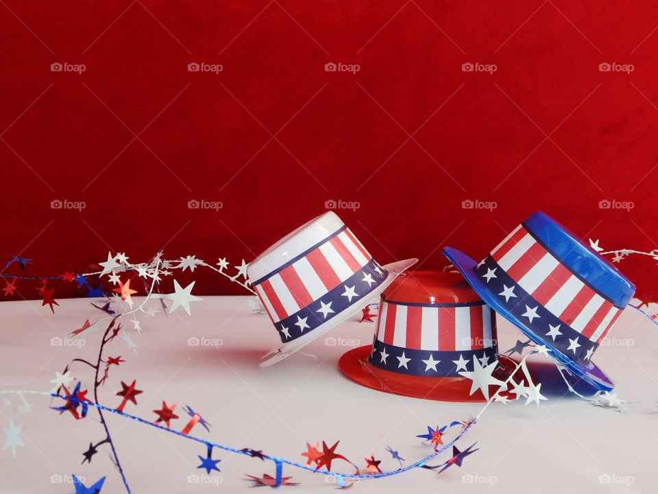 Tiny party hats in red, white, and blue with the Stars and Stripes for hat bands on a table with confetti. 