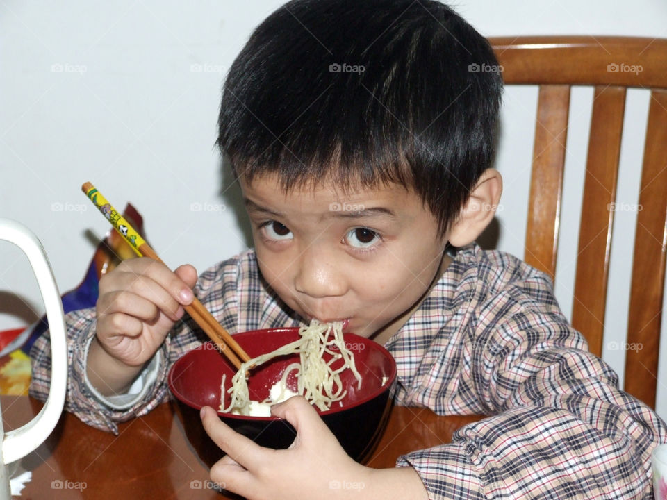 Little boy eating delicious noodle with chopstick