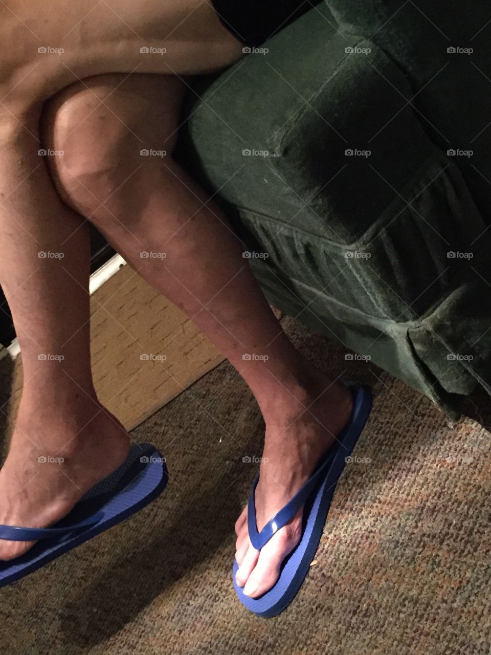Mans legs with blue flipflops in a chair. Can only see legs flip flops and rug.