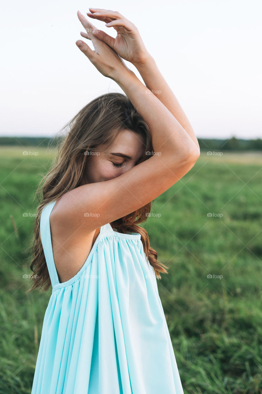 Close up portrait of Young beautiful carefree long hair woman in light blue turquois dress in sunset field. Sensitivity to nature concept feminity