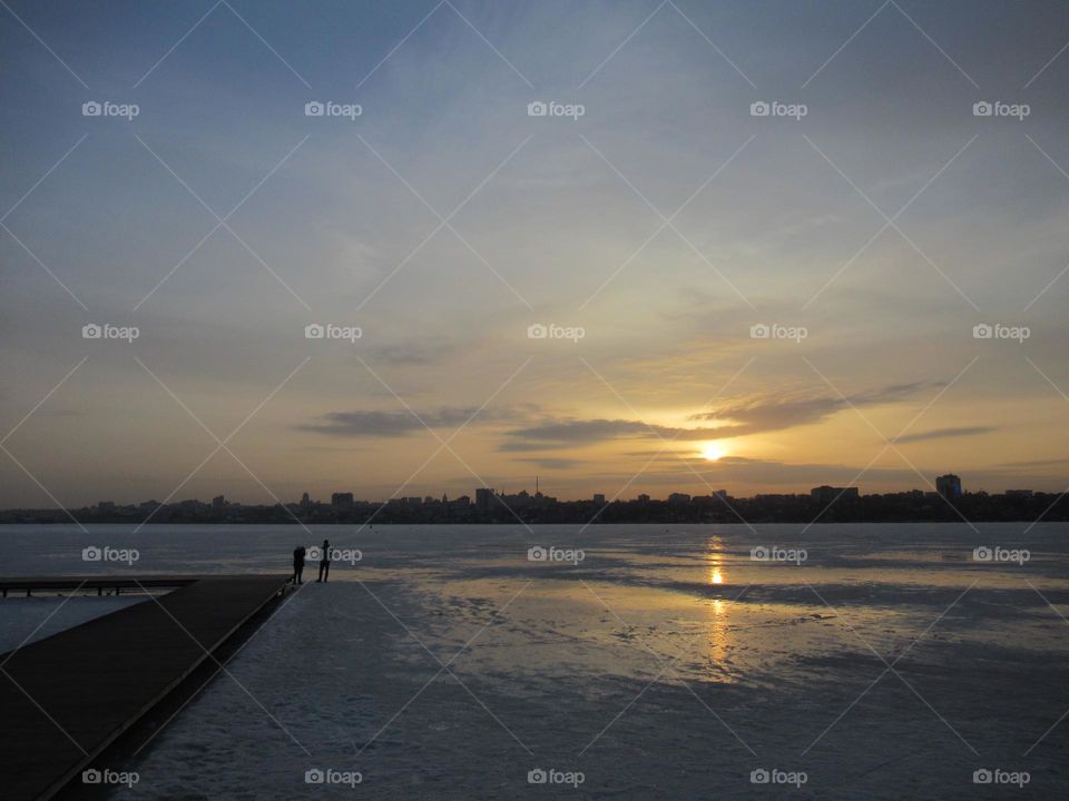 sunset in March, the ice on the river is not melting yet, but walking is dangerous, the sky is cloudy, the sun is shining