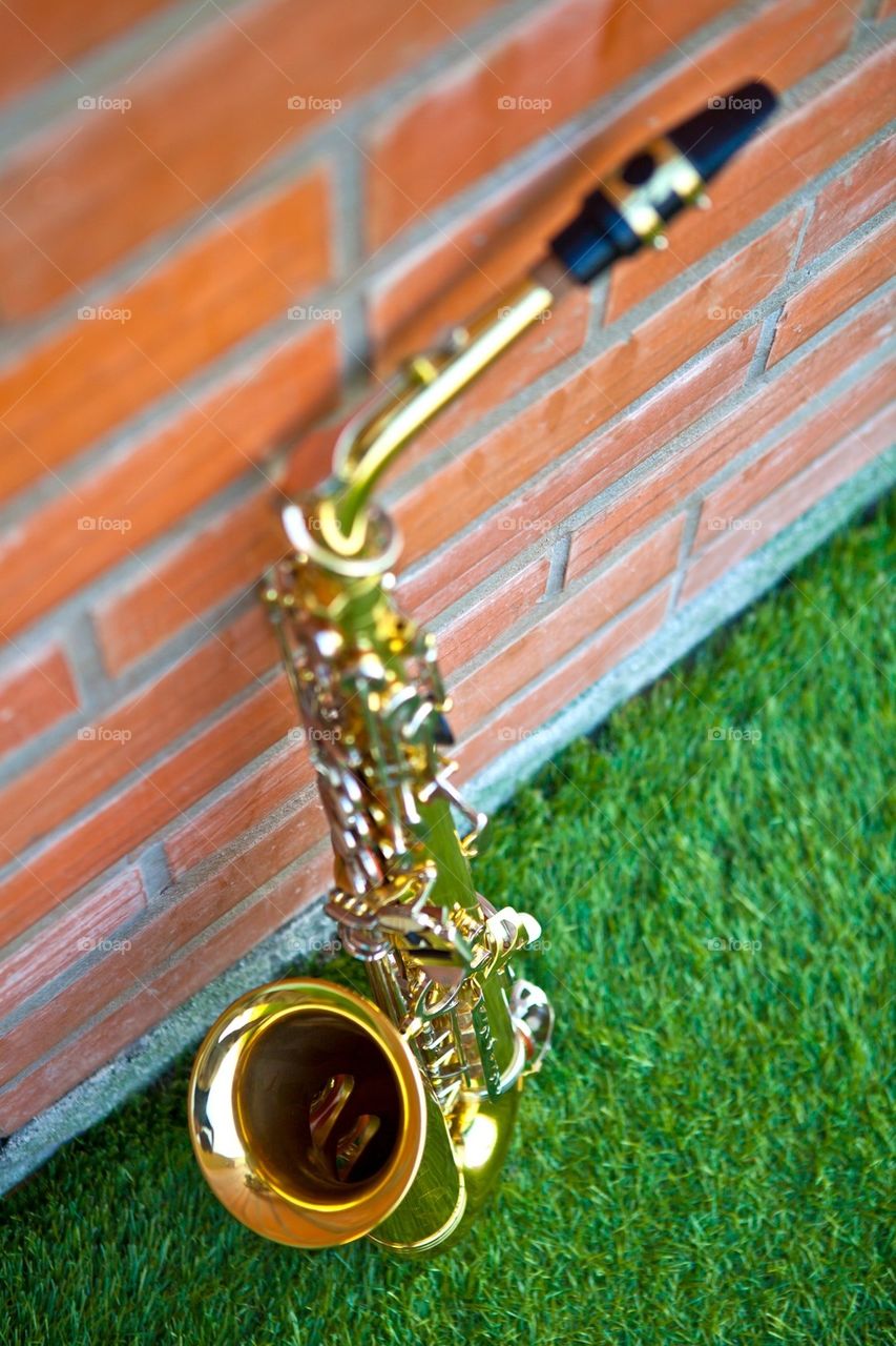 Saxophone lean against brick wall on green grass