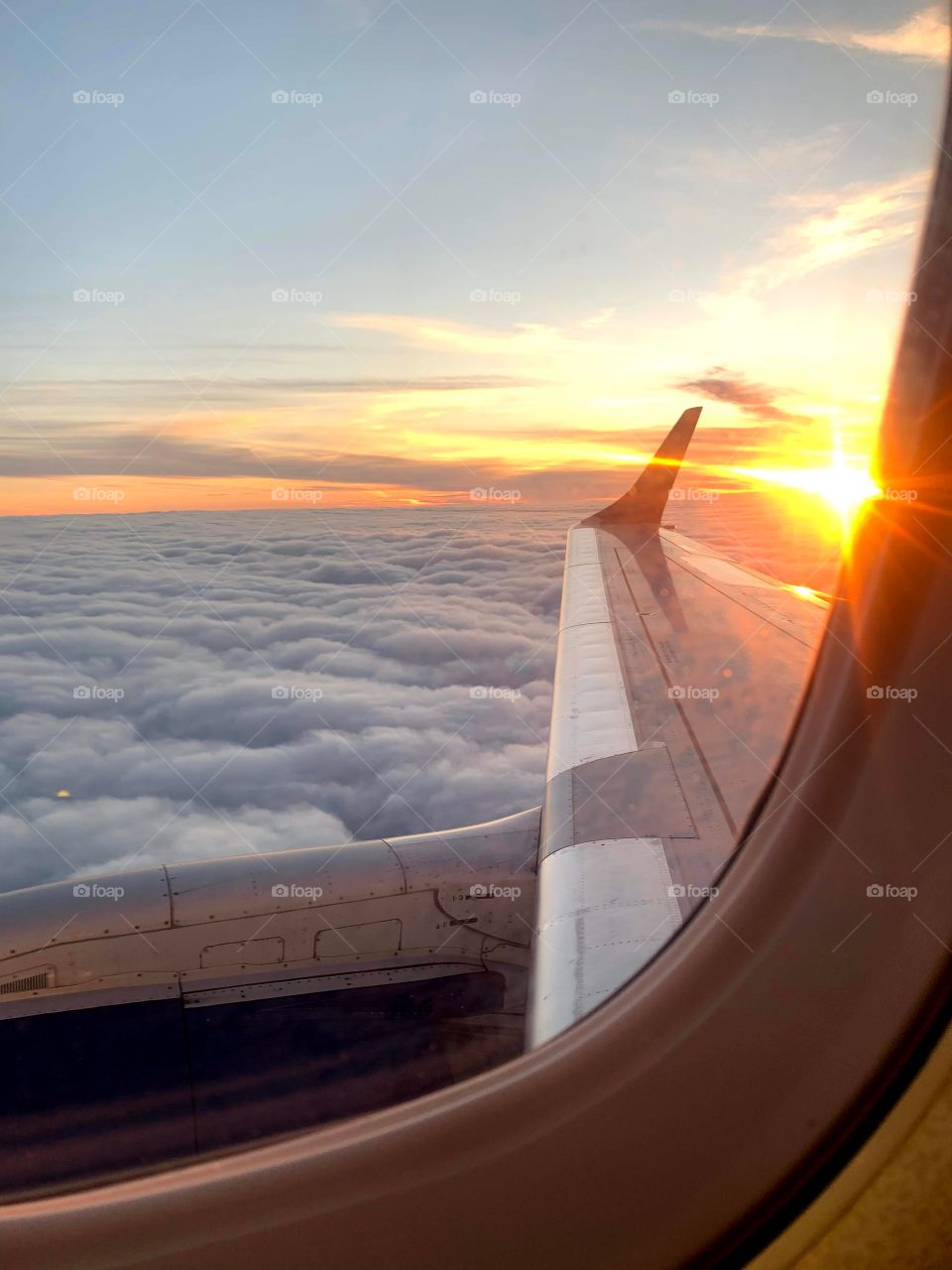 Looking out airplane window to the wing clouds and sunset in the distance