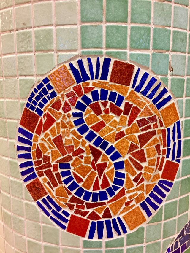 Letter S mosaic in red orange and blue tile chips on a pillar
