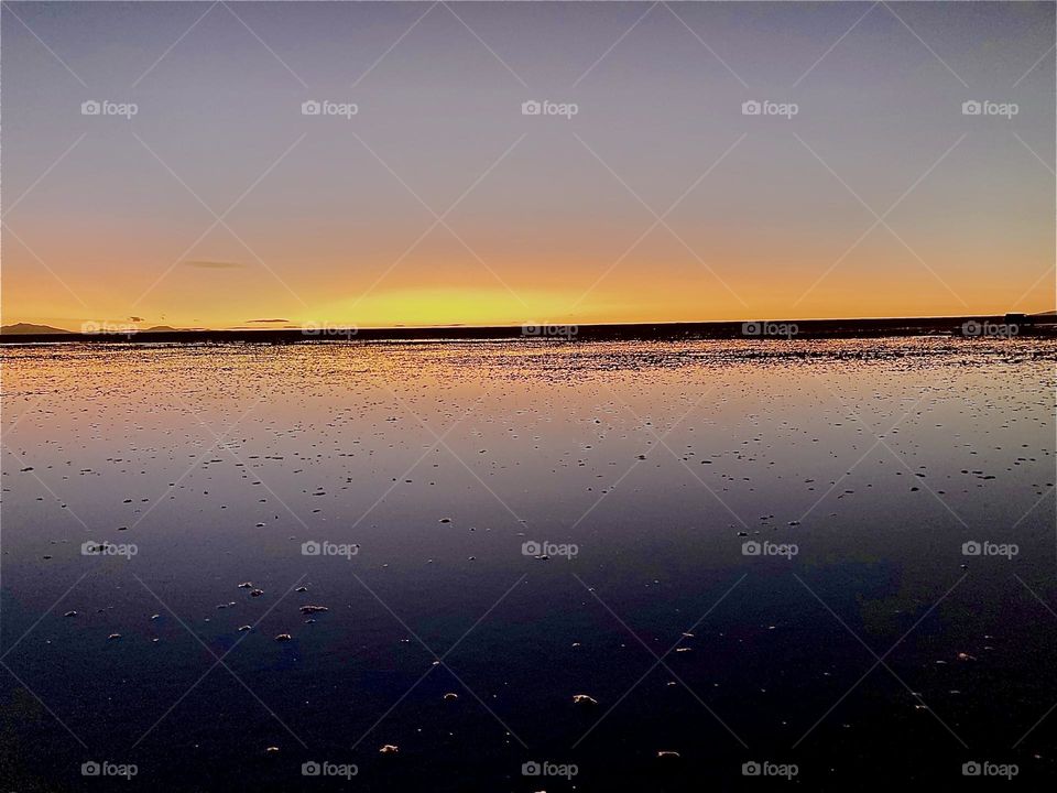 The sun is setting at the horizon over the “Uniyuni Salt Lake” in “Bolivia” in “Central America”. It is almost twilight time and nightfall is near. 2022. Hypnotic Productions