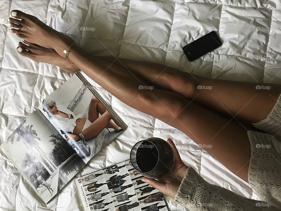 Home relaxation in cozy bed with red wine and fashionable magazines and mobile phone 