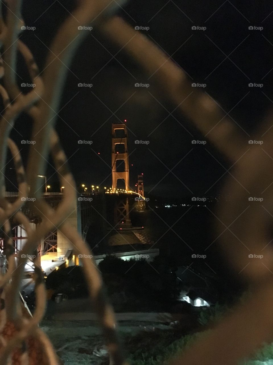 Golden Gate Bridge in San Francisco at night through a chain link fence