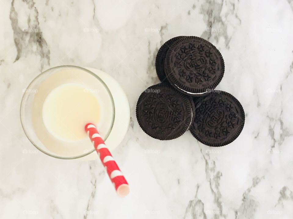 Chocolate double stuff Oreo cookies and a glass of milk with a red and white straw on a marble background