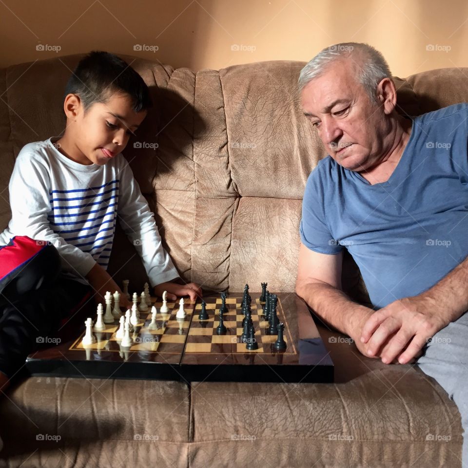 Young boy is playing chess with his grandfather at home