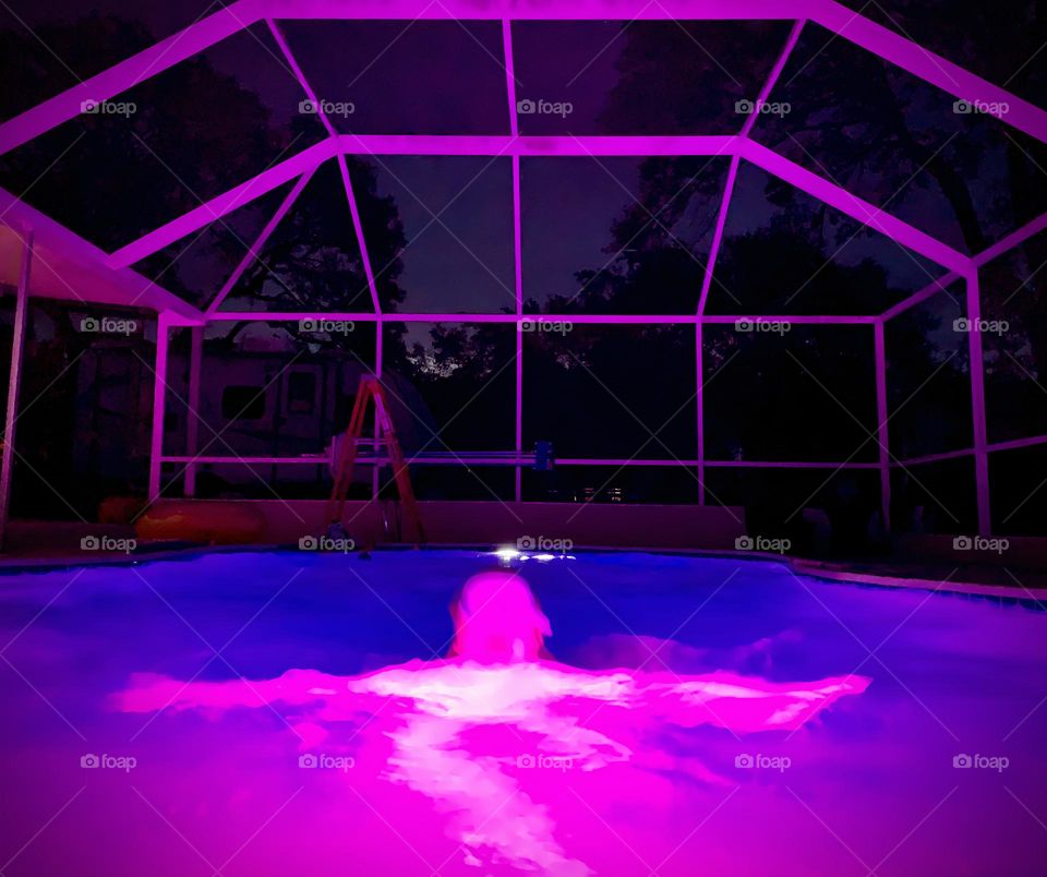 Purple Light Lighting Up The Pool And The Enclosure Around It With Swimmer In The Middle With Pink.