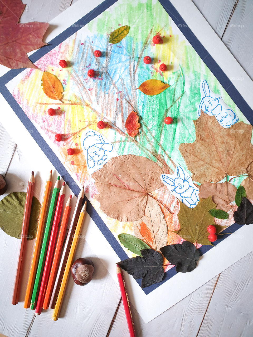 Children's creativity.  Crafts, children's painting, application with autumn leaves and mountain ash on a light wooden background with chestnuts, multi-colored dry leaves and pencils