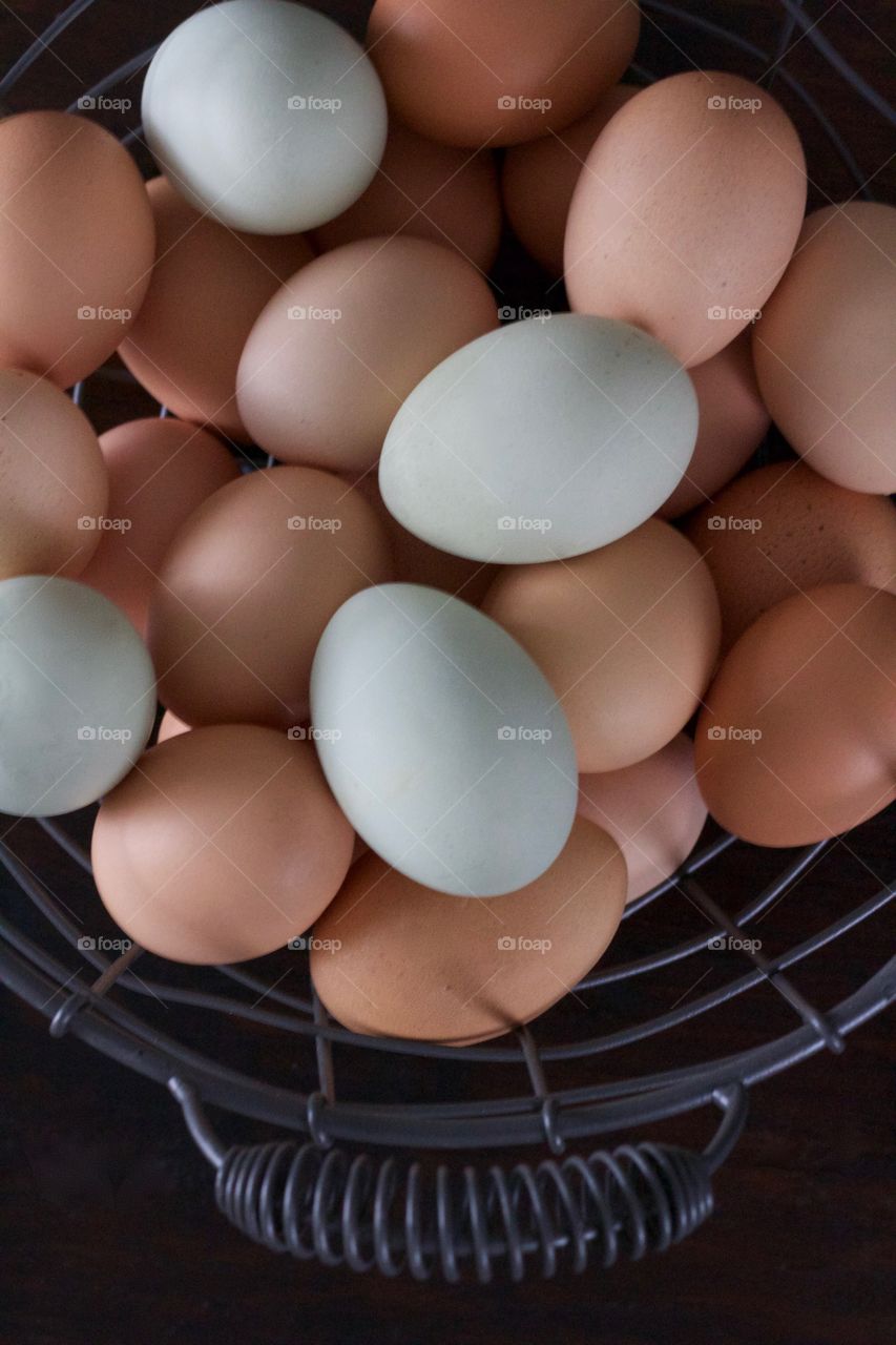 Overhead view of farm-fresh blue and brown eggs in a wire basket on a dark wooden surface