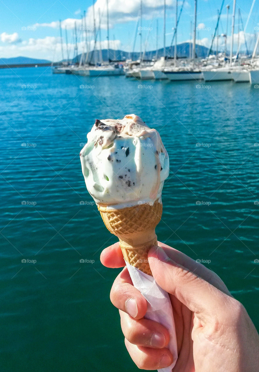 Person's hand holding ice cream in front of sea