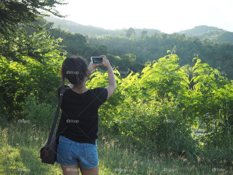 girl take a photo with forest among natural under the lighting of sun at green valley