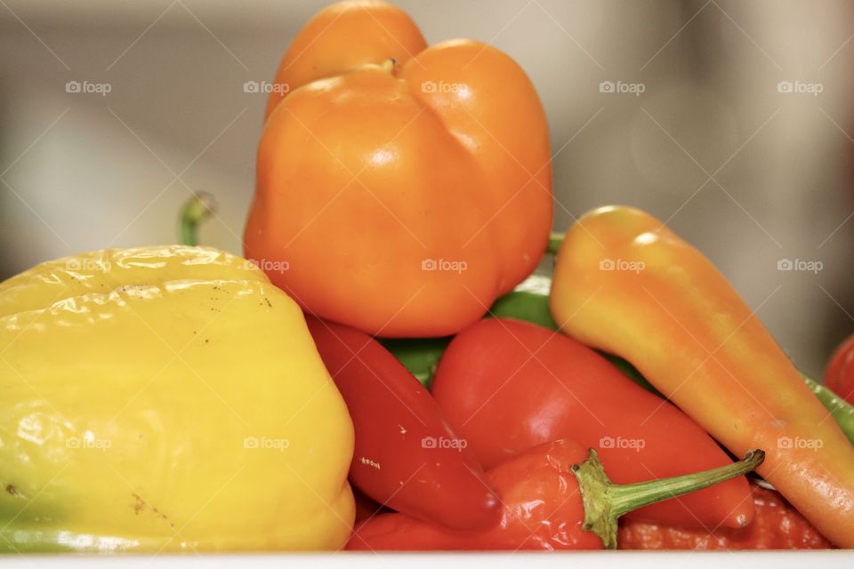 Bright orange sweet bell pepper capsicum atop a pile of multi coloured peppers still life 