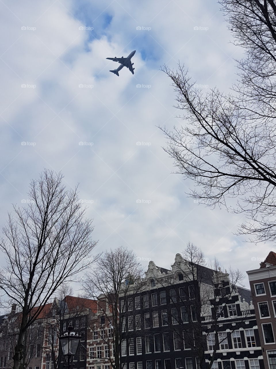 Vintage architecture roofs on buildings on an old alley street in Amsterdam, Holland, Europe. Airplane jet in clouds sky flying above