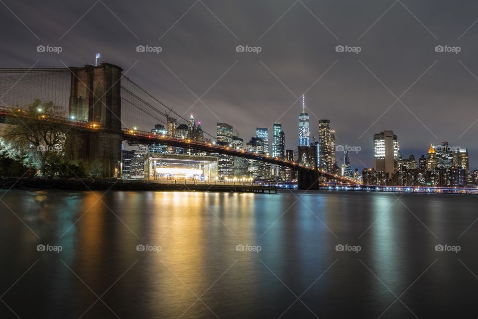 New York City skyline behind the Brooklyn bridge at night.
