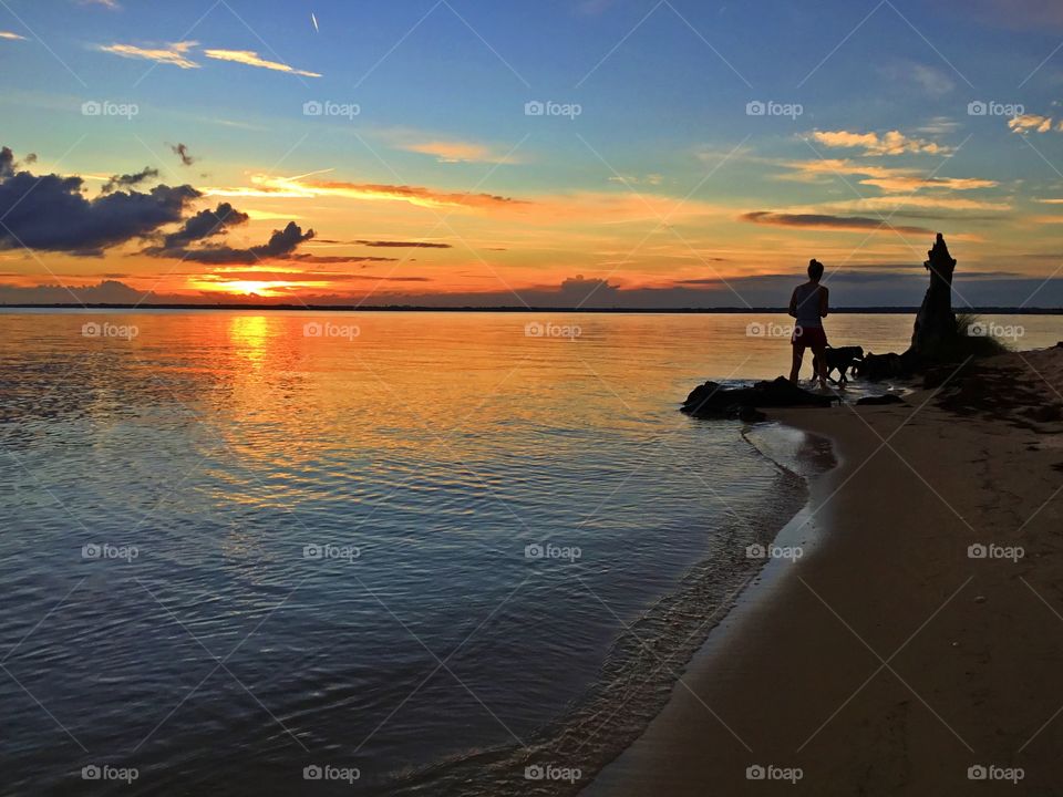 A girl walking her dog around edge of the beach during a magnificent sunset evening