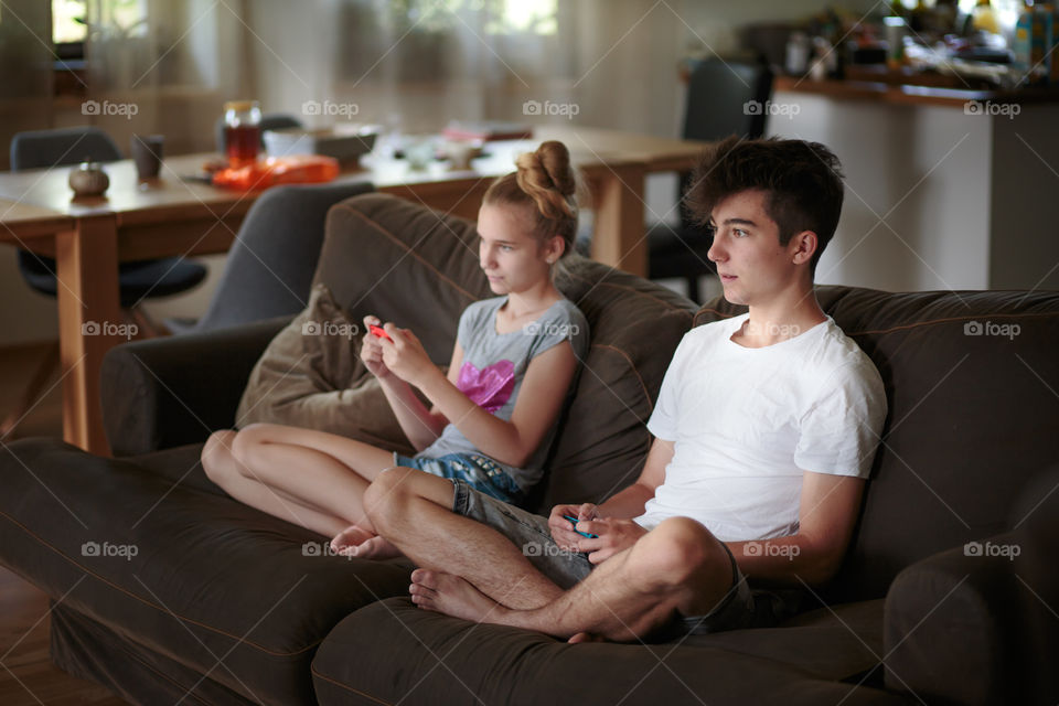 Concentrated young boy and girl playing video games sitting on sofa at home