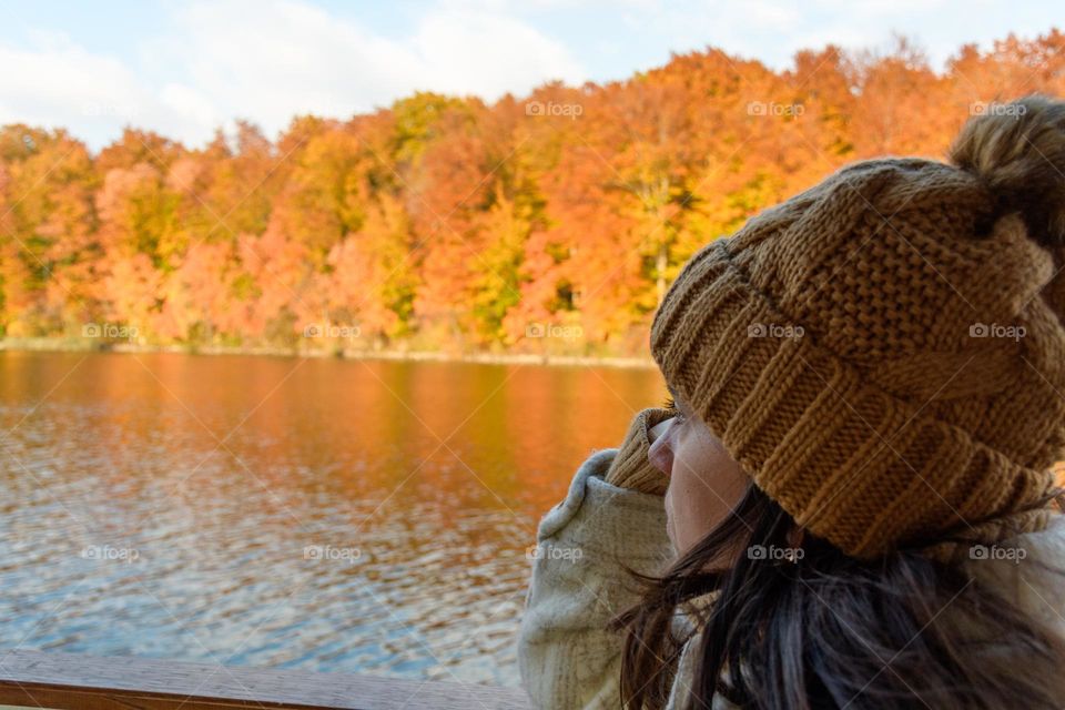 Side view of young woman on tourist boat on lake. Beautiful autumn forest on shore of lake at Plitvice lakes national park in Croatia.