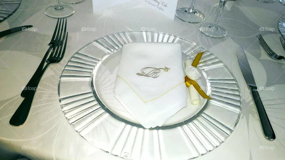 A glass plate with cutlery, a napkin and a wedding place card decorated with a yellow ribbon