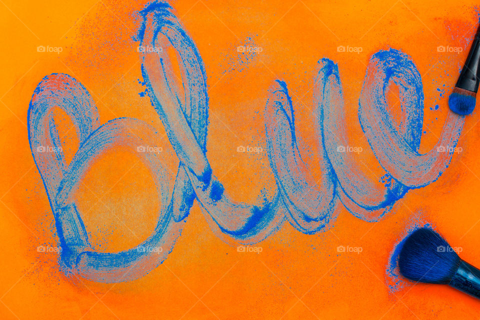 orange and blue - image of word blue and make up brushes with blue powder and orange background