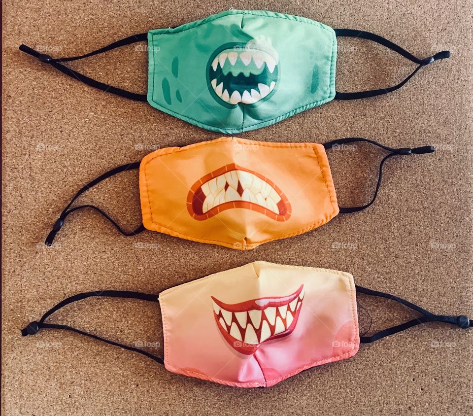Three face masks with silly faces of vampire sharp teeth during the world wide pandemic 