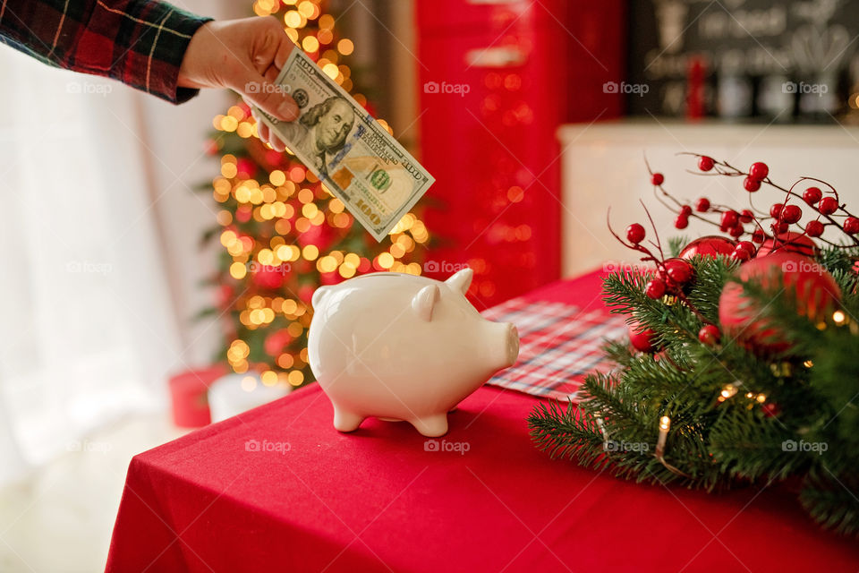 piggy bank with 100 dollars banknote in festive New Year atmosphere of scenery.  Magical bokeh with Christmas tree and bright lights.