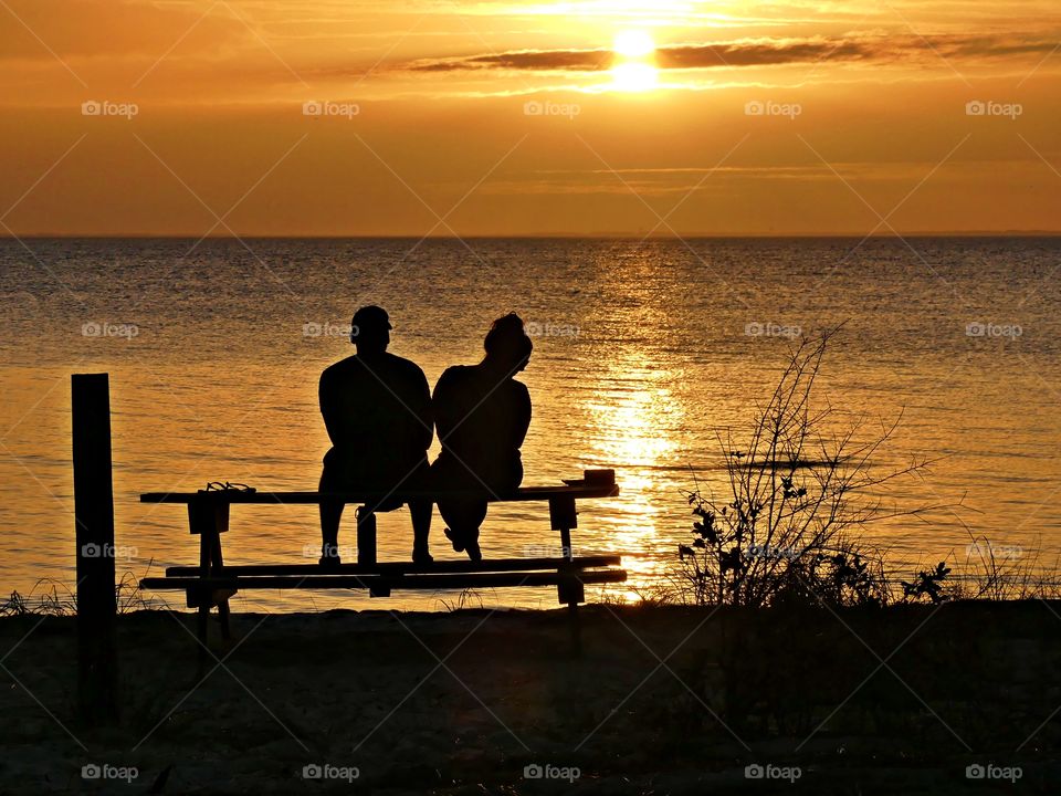 
Even numbers -  A romantic couple sitting on a picnic table watch a magnificent sunset descending over the shimmering bay.