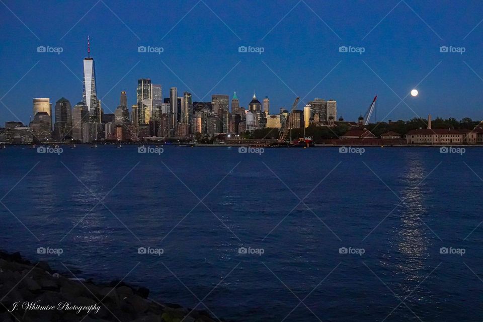 A full moon rises on a crystal clear fall evening with the glow of the Manhattan skyline in the foreground