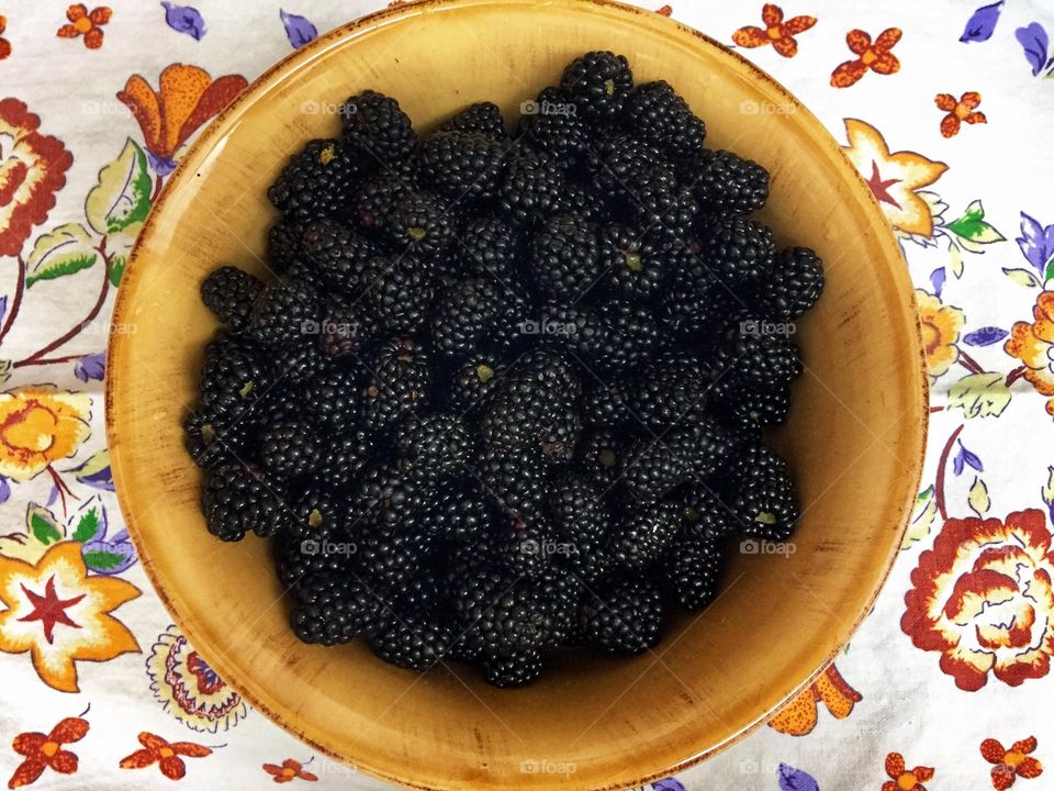 Yellow ceramic bowl full of plump fresh-picked blackberries displayed on a colorful cloth