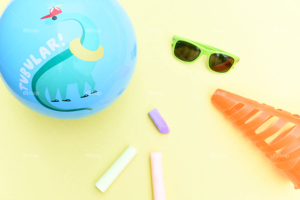 Flat lay of brightly colored summer objects including sidewalk chalk, sunglasses and a ball