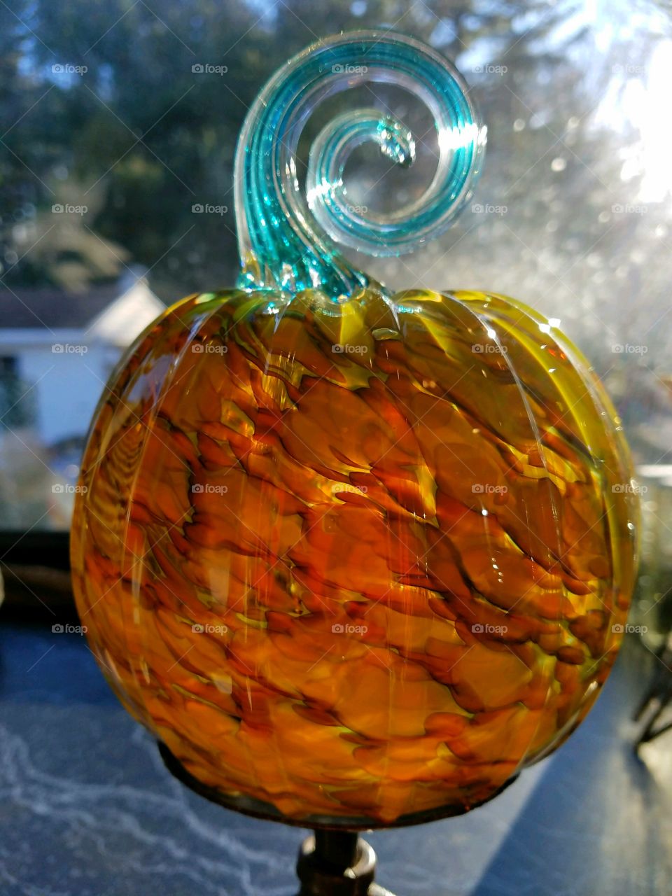 Glass hand blown pumpkin, sun is  shining through shades of colors, with a fancy spiral shape blue stem.