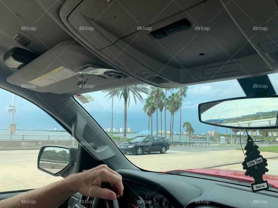 Commuting: driver man holding the steering wheel driving on the road before a storm y the Indian lagoon in Florida.