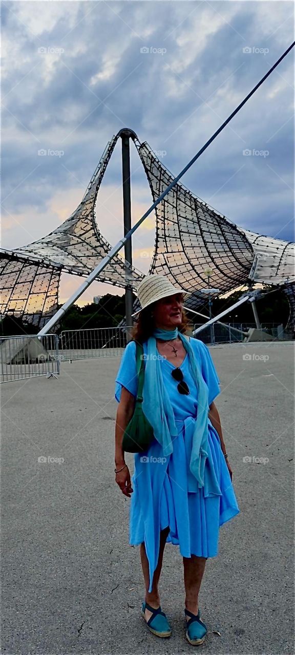 The futuristic shapes of the stadium for the “1972 Olympics” in “Munich” combine well with the antique Greek or Roman inspired high fashions our model is wearing in the foreground that are wrapped much like a toga. 2024. Hypnotic Productions