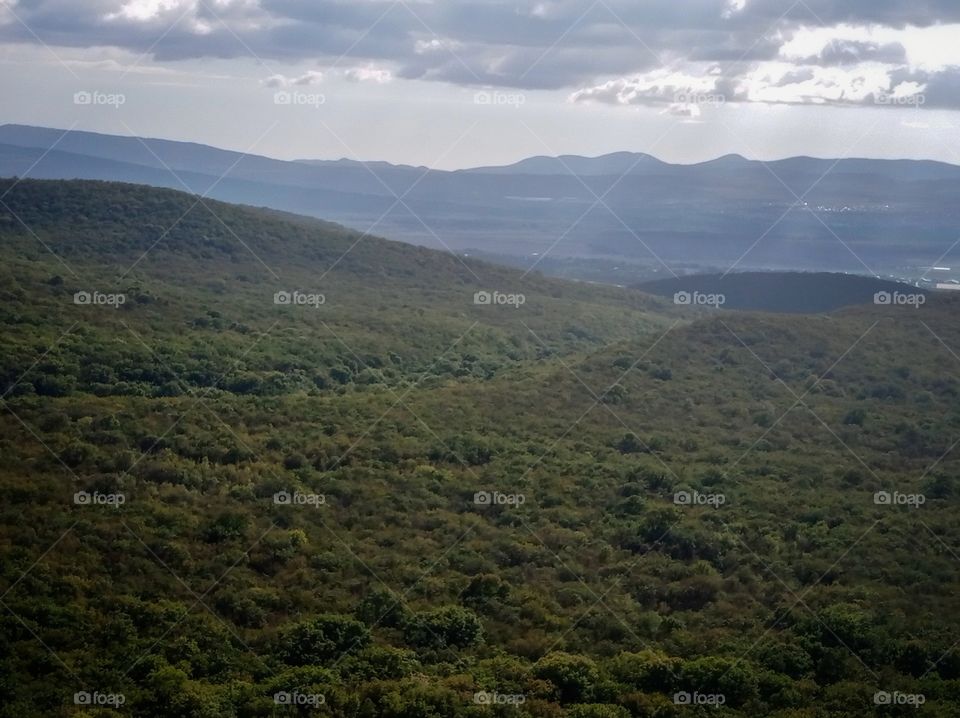 Mountains and forests. The sun's rays shine through the clouds.