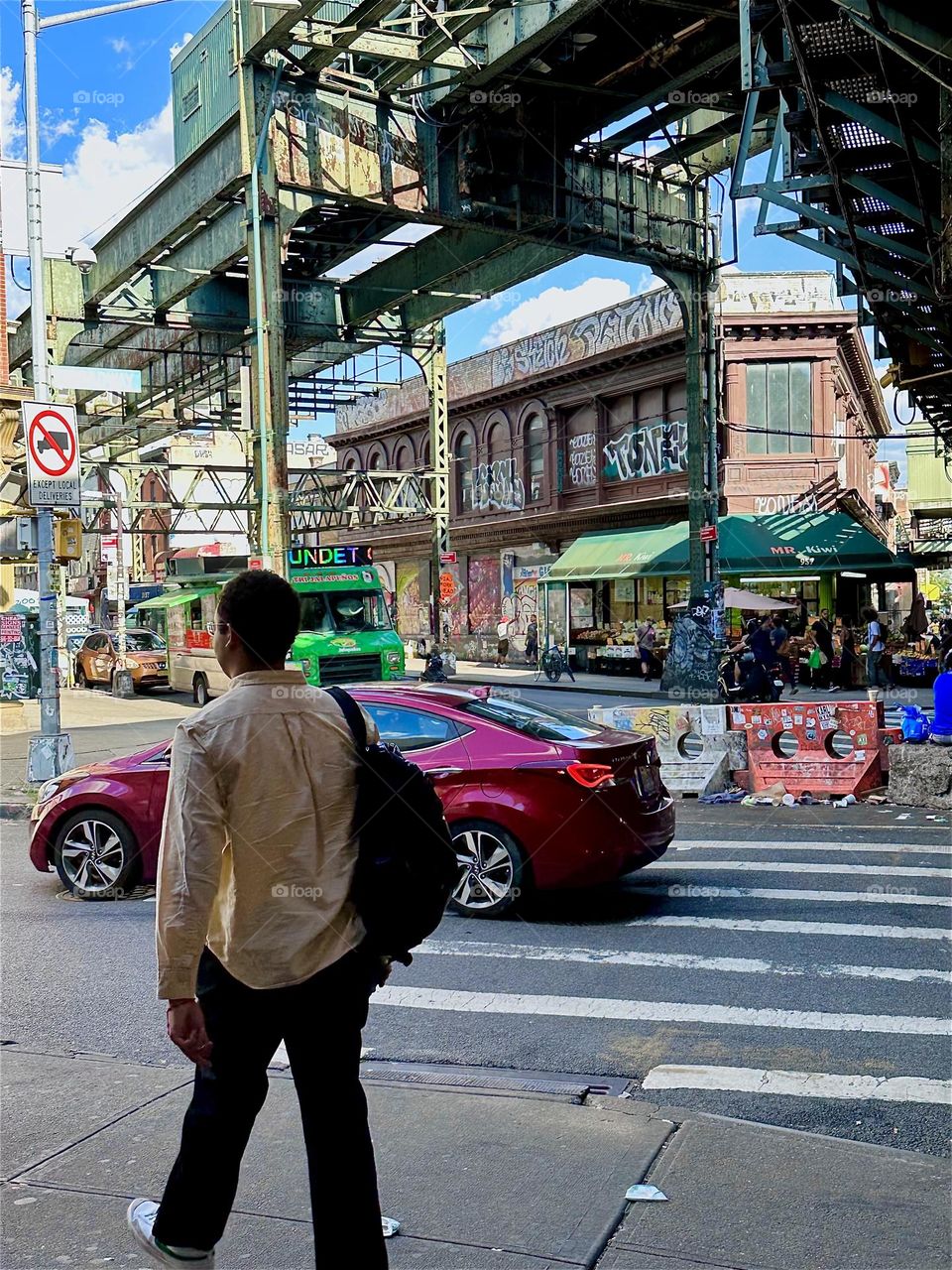 This gentleman is walking down “Broadway” at “Myrtle Ave” in “Bushwick”, Brooklyn. Above two overpasses intersect diagonally with the “Broadway” overpass housing the MTA “M” train. 2024. Hypnotic Productions