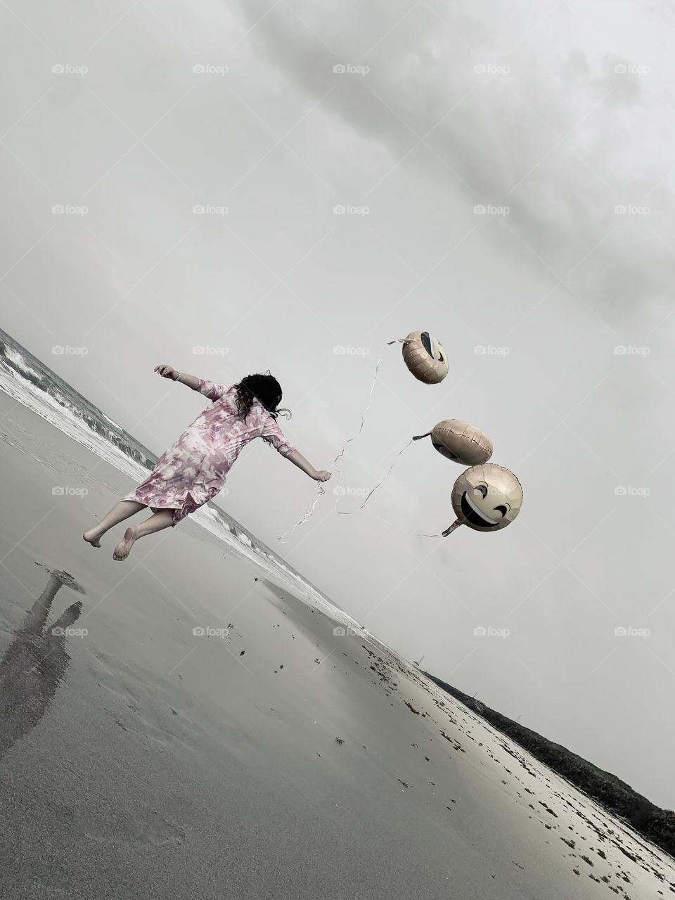 Little Girl Seems To Be Flying And Carried Up In The Air By The Three Helium Emoji’s Balloons On The Beach By The Ocean.