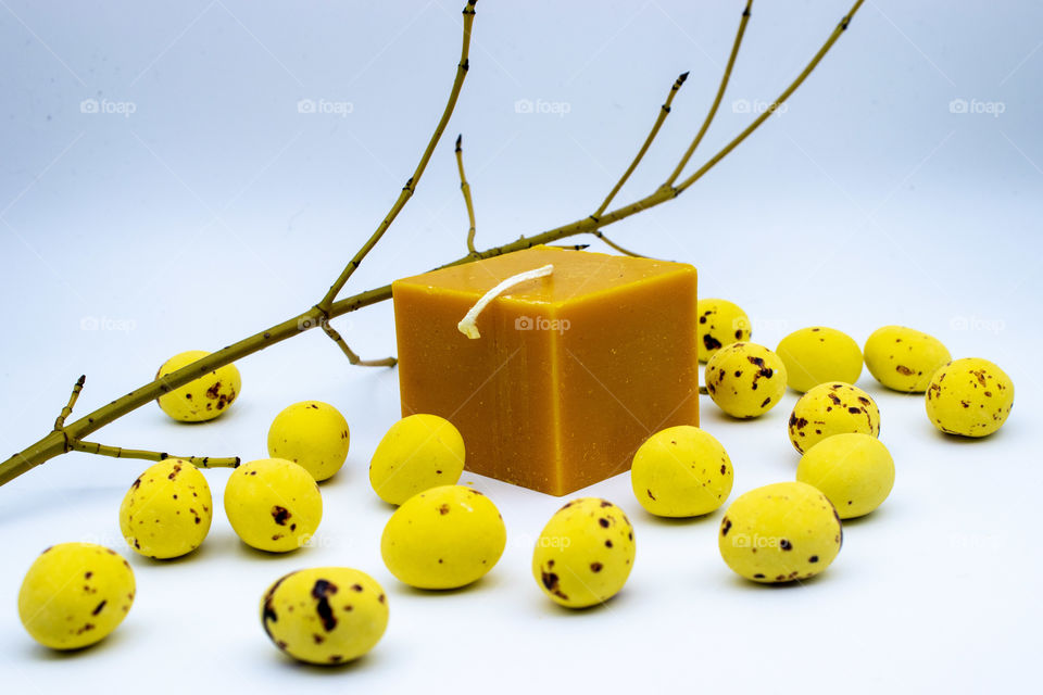 Yellow brick candle with yellow chocolate Easter eggs scattered around. Bloom spring branch in the background