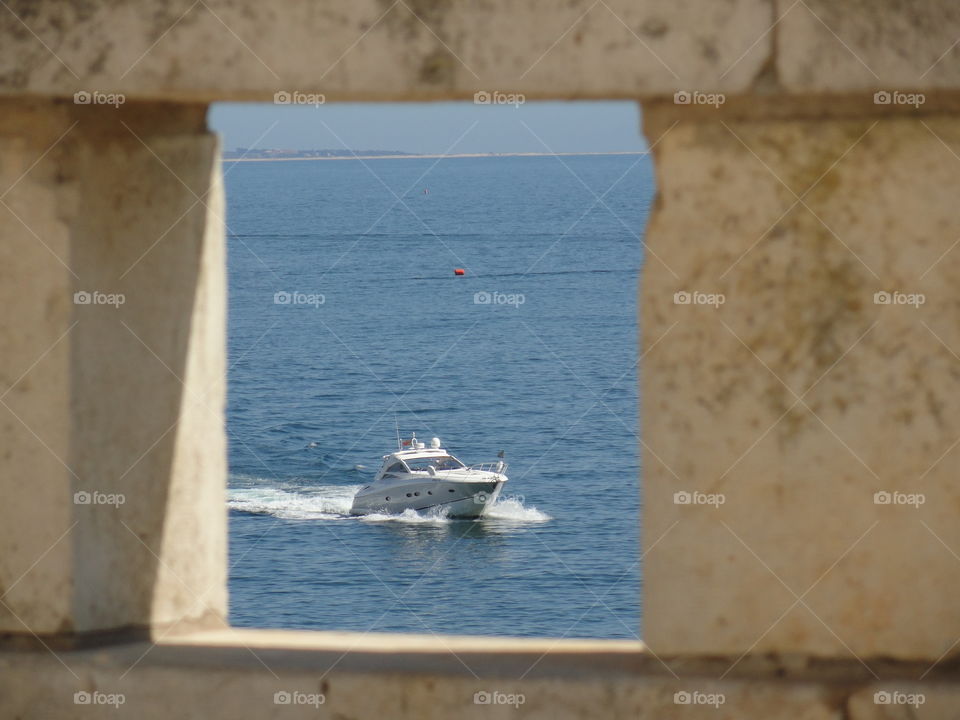 A portrait of a speedboat in the sea sailing by, captured through a hole in a wall.