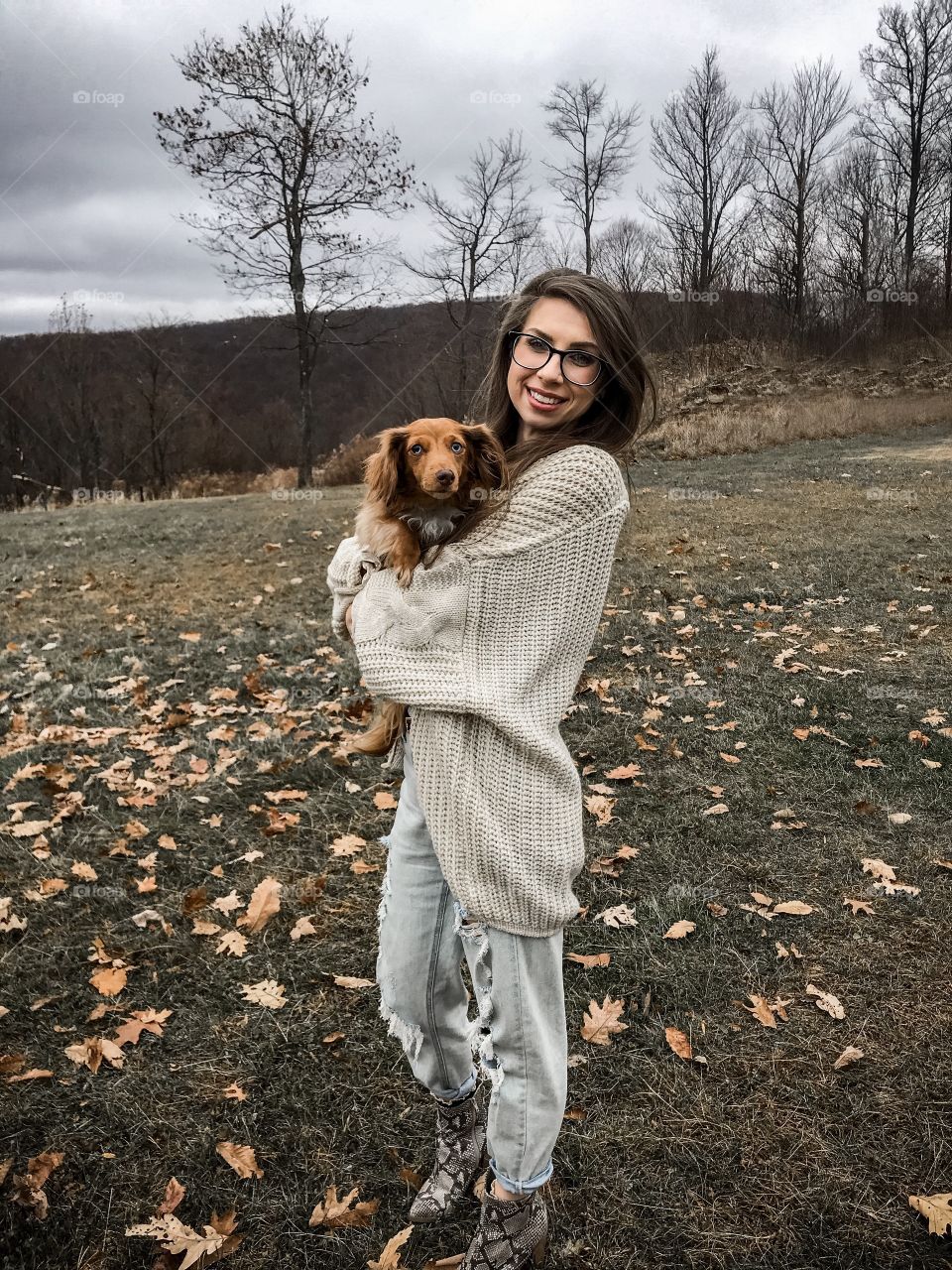 Brunette girl in autumn holding mini long haired dachshund outdoors with leaves and fall foliage 